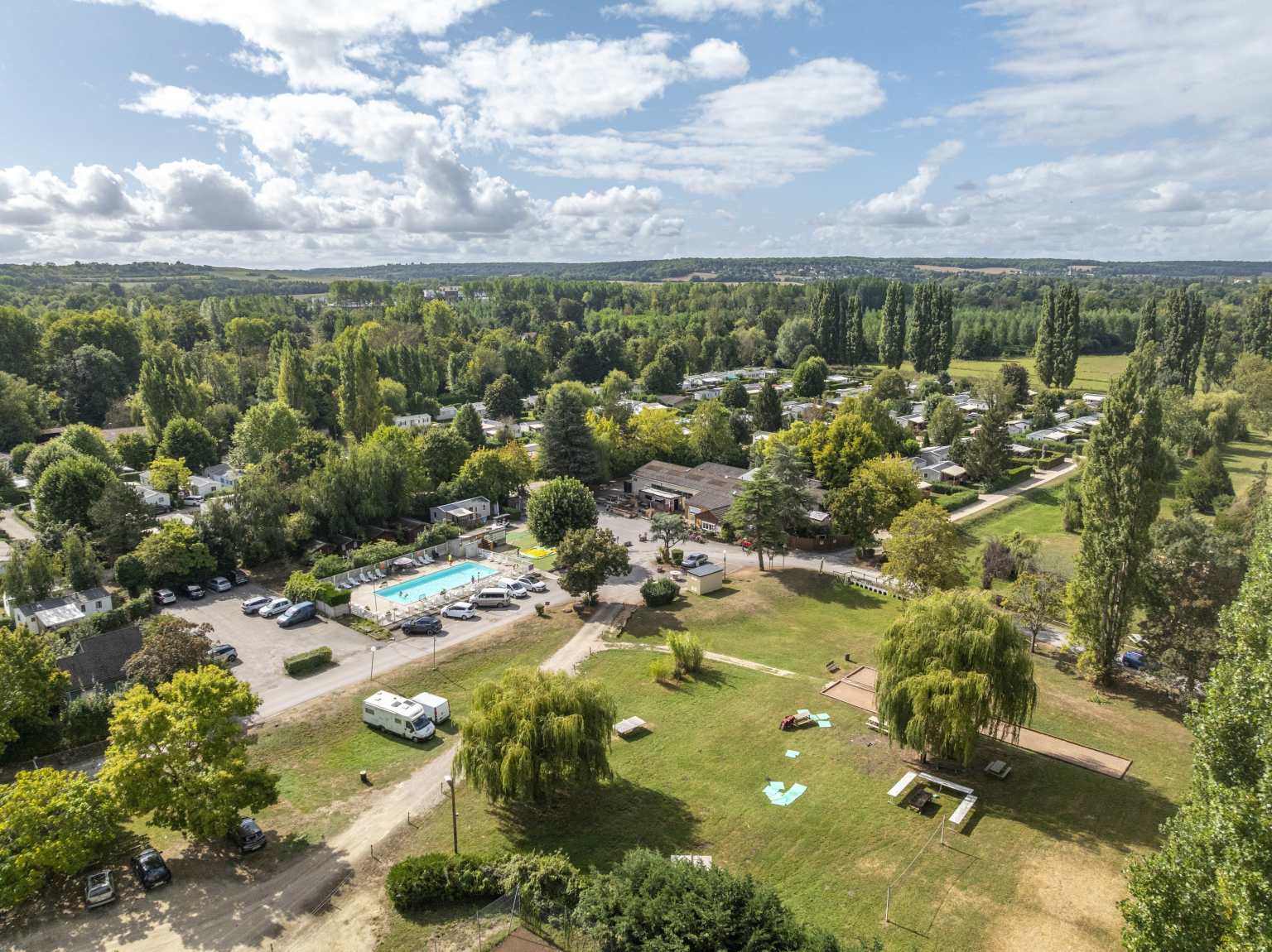 Aerial view of the swimming pool, open grassy spaces and wooded pitches at Les Fontaines campsite, Ivry-la-Bataille, France