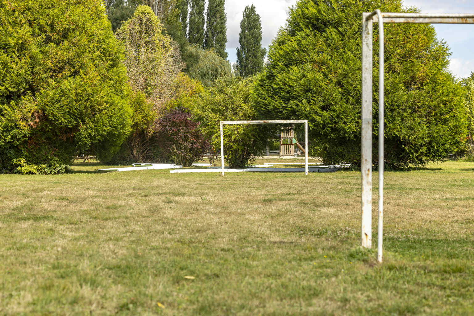Grass football field with goal posts, surrounded by tall trees, at Les Fontaines campsite, Ivry-la-Bataille, France