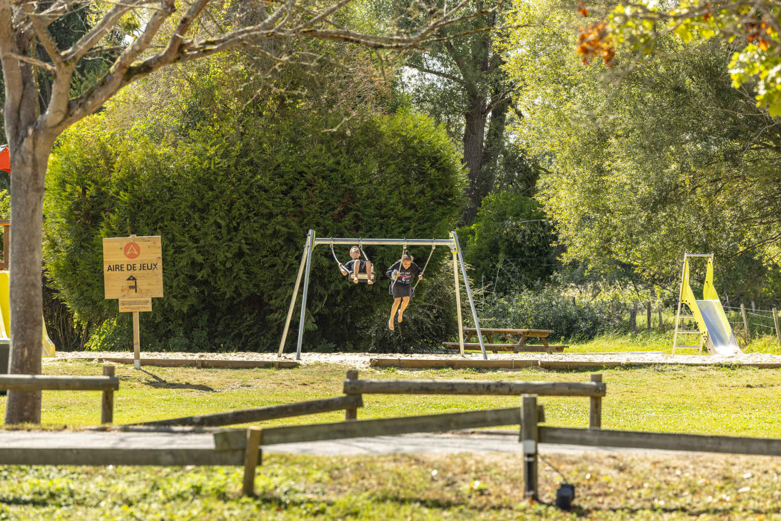 2 children on the swings in the play area at Les Fontaines campsite, Ivry-la-Bataille, France