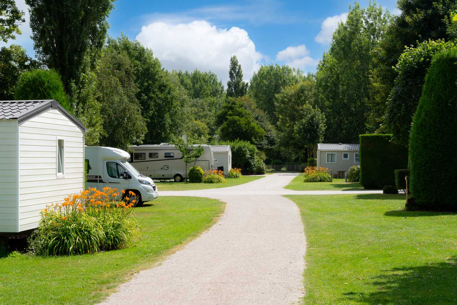 Holiday homes opposite camping pitches, separated by shrubs and trees at La Bien Assise campsite, Guines