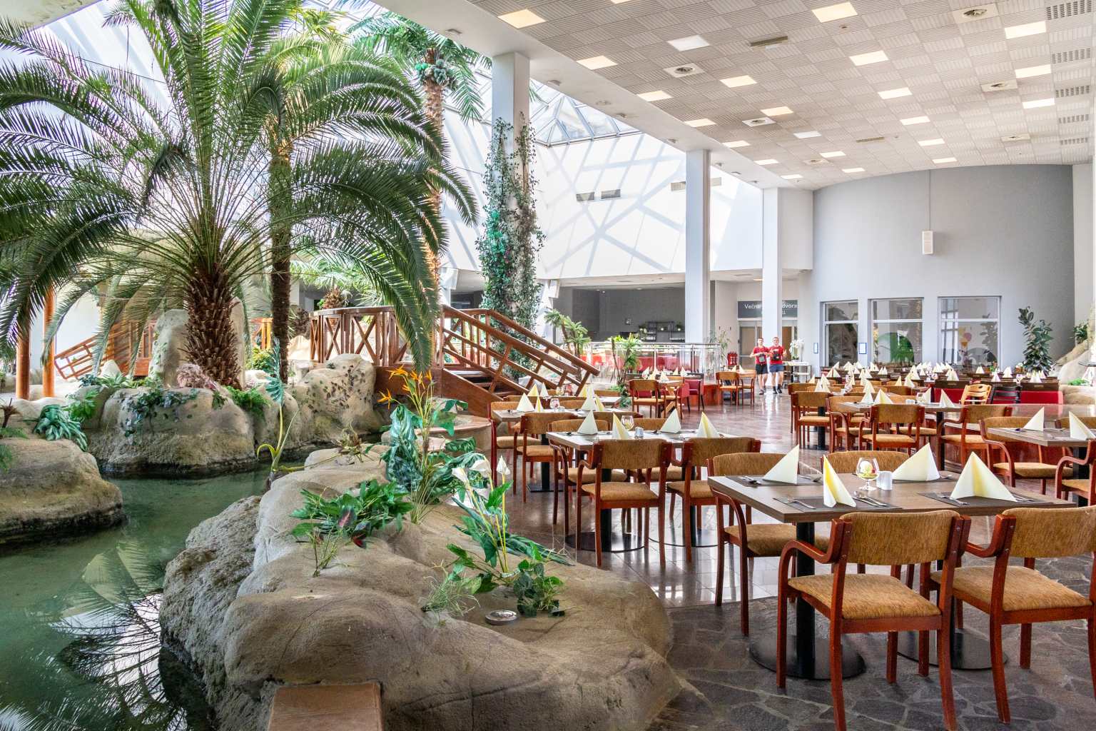 Restaurant tables next to palm trees and indoor stream at Terme Čatež campsite in Slovenia