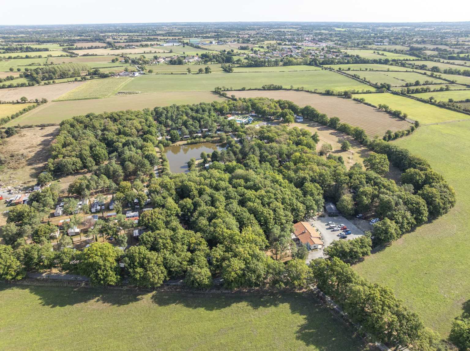 Aerial view of the fields and woods surrounding the lake at the centre of Coeur de Vendée campsite, in France