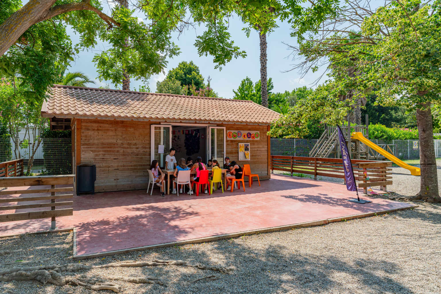 Kids sat at a table outside the Fun Club wood chalet with animation leader at la Sirene campsite in the Roussillon