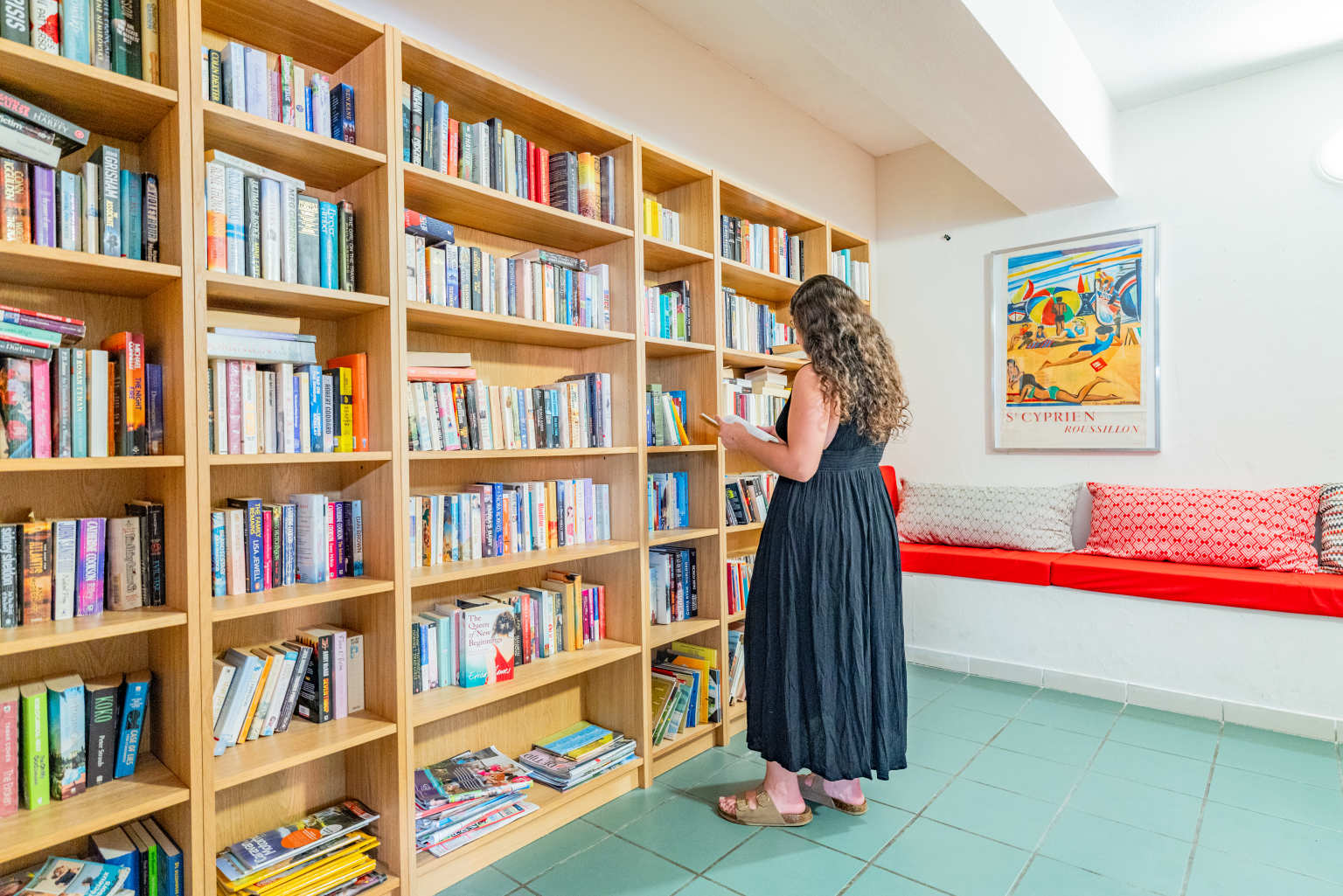 Lady looking at books on the wall of shelves at the onsite library at Ma Prairie campsite in the Rousillon, France