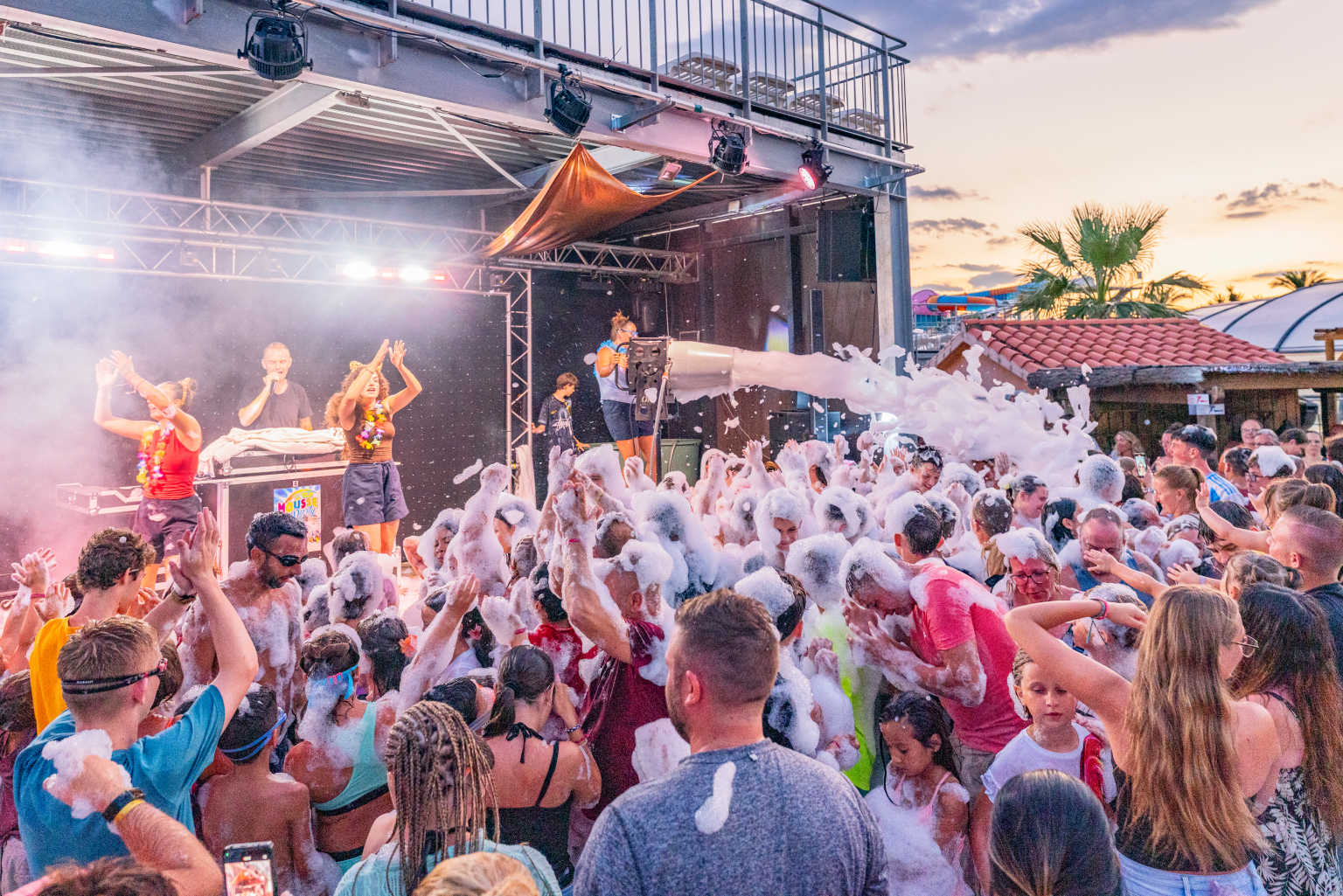 Foam cannon firing above the crowd at an evening party under the palm trees at le Soleil de la Mediterranee campsite, Roussillon