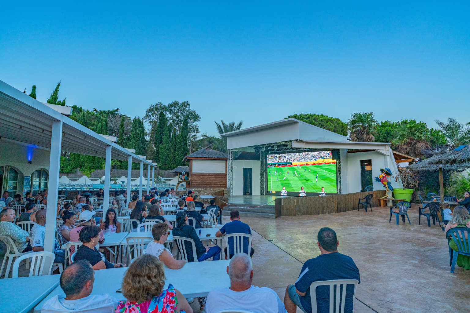 People sat on the restaurant terrace at night watching football on the huge outdoor screen at La Croix du Sud campsite in the Languedoc