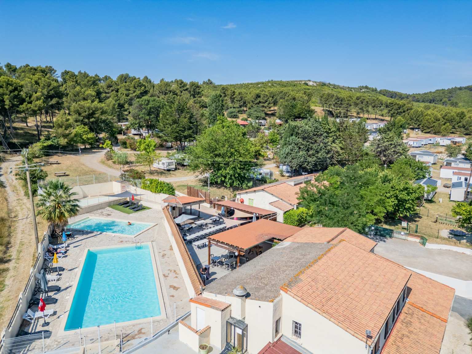 Aerial view of small rectangular family pool, at an angle, a rectangular kids pool, buildings to the right, trees in the distance, at Borepo campsite, Languedoc