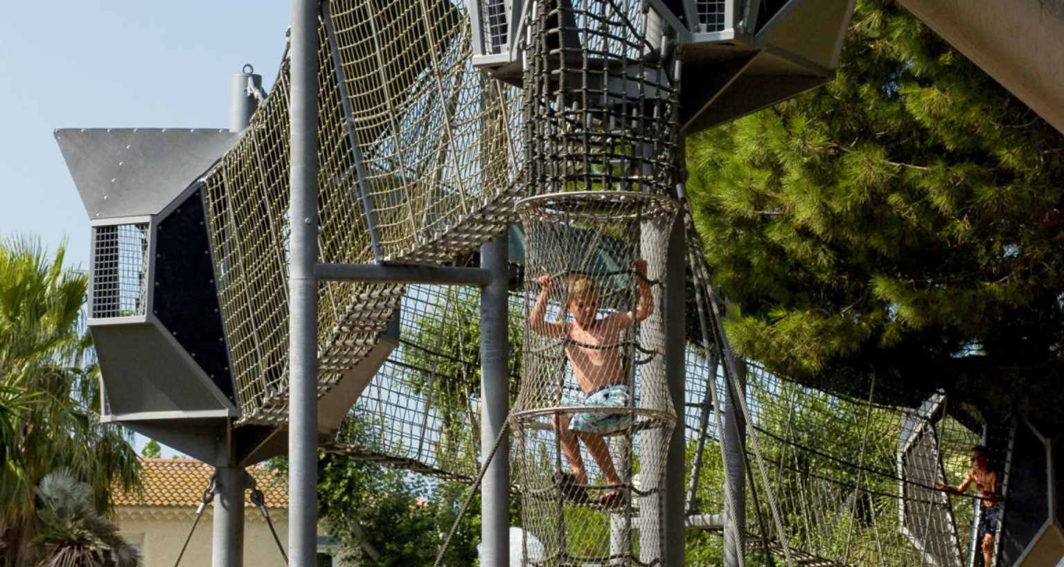 Boy climbing through the nets and rigging in the suspended high ropes adventure course at Les Sables d'Or, campsite in the Languedoc
