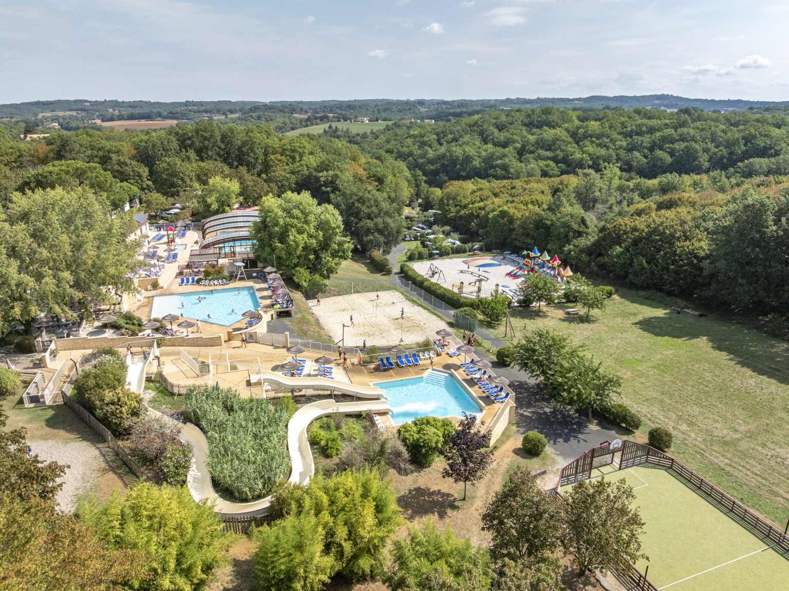 Aerial view of pool complex and fields and woods around Les Truffières de Dordogne campsite near Souillac