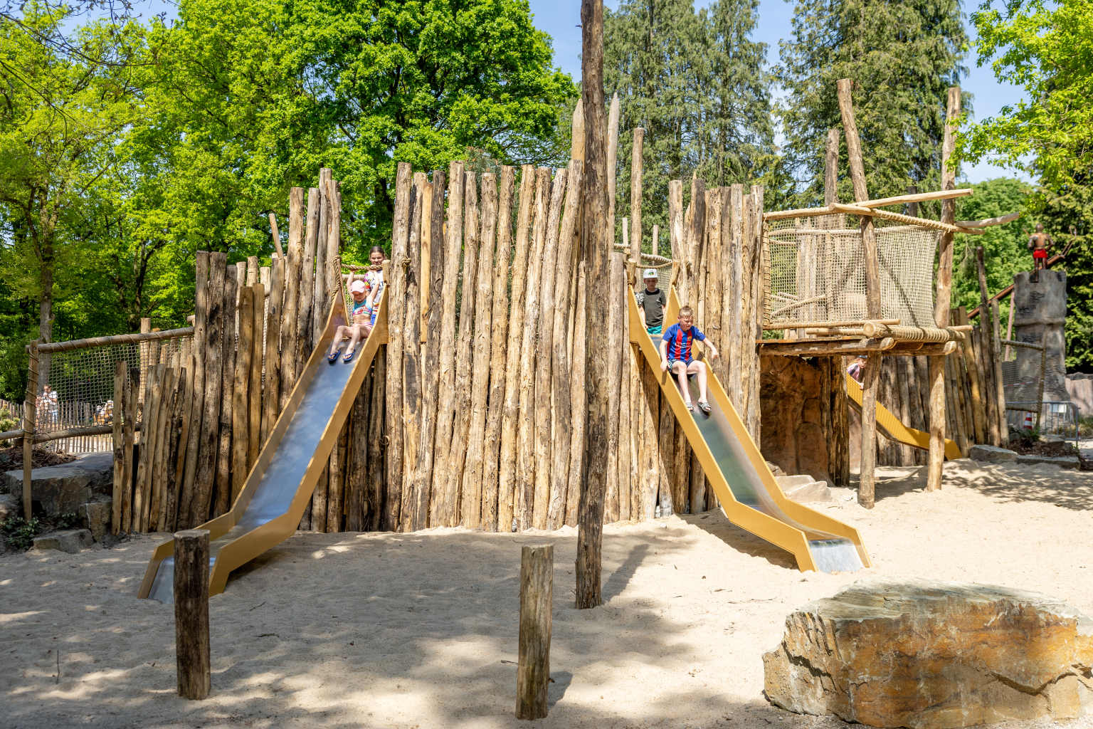 4 kids going down the 2 slides at the outdoor wooden play area at Vakantiepark de Bergen campsite in the Netherlands