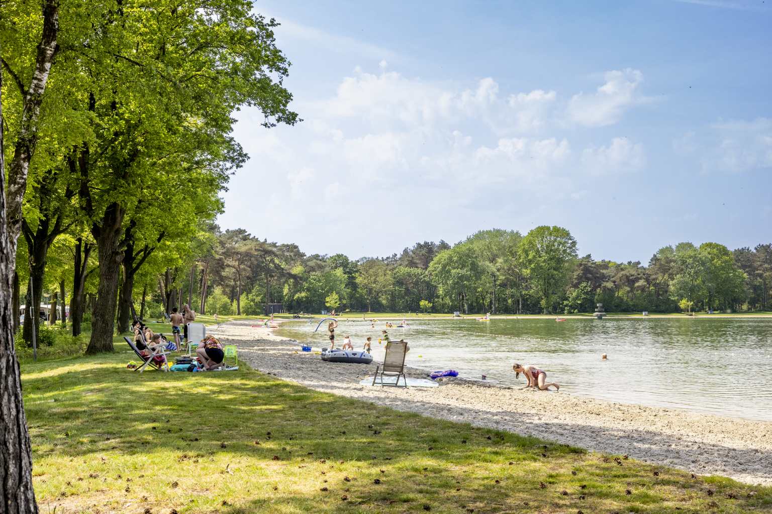 Families sunbathing by the lake beach at Vakantiepark de Bergen campsite in the Netherlands