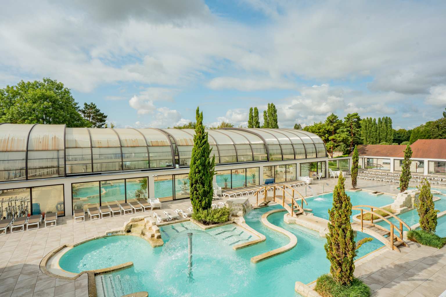 Aerial view of the outdoor pool, with large trees on the poolside and wooden bridges to cross at La Croix du Vieux Pont