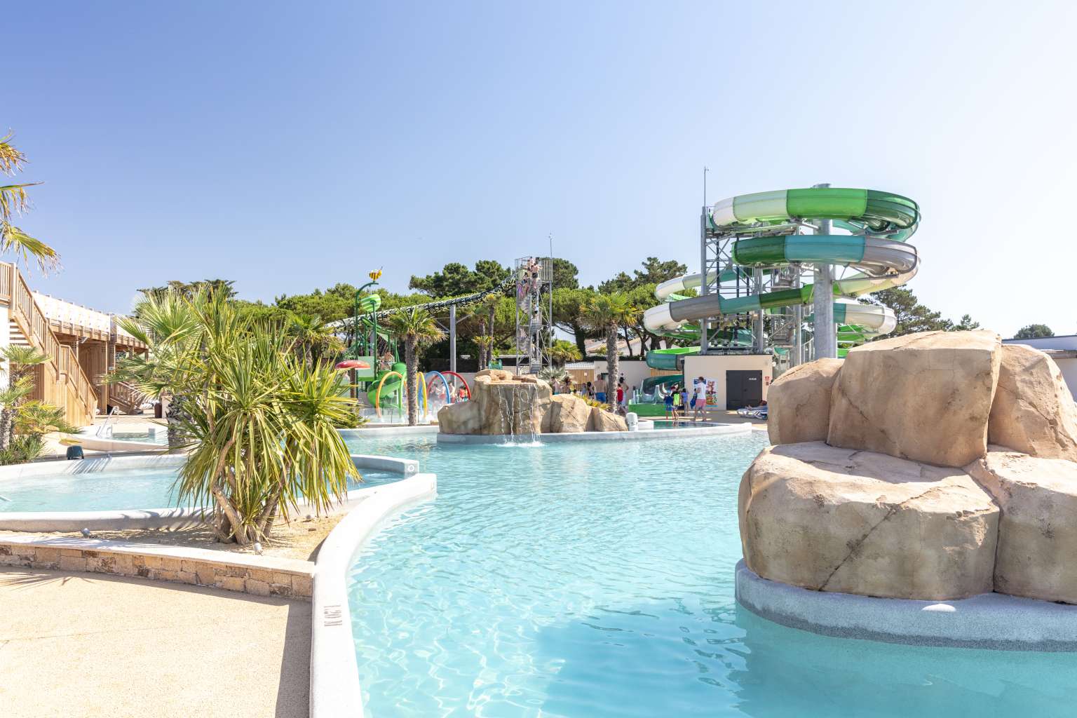 View of the pool complex, with a large stone section within the pool, showing the twisty slides in the background on Le Domaine du Clarys - Le Clarys Plage