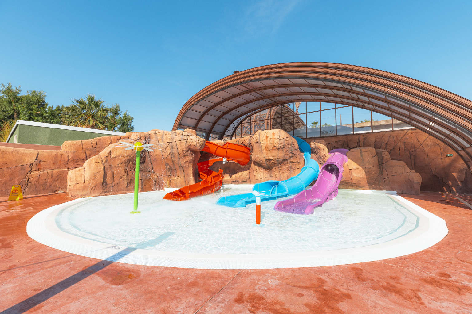 Kids waterslides built into the faux rock face in the covered pool (canopy open) at la Sirene campsite in the Roussillon