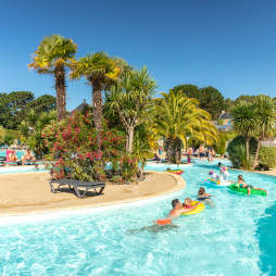 Parents and kids floating in the lazy river under the palm trees at la Grande Metairie campsite near Carnac in Brittany