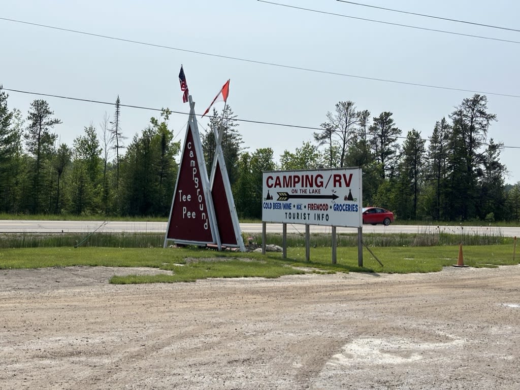 Camping signs near a road with trees in the background.
