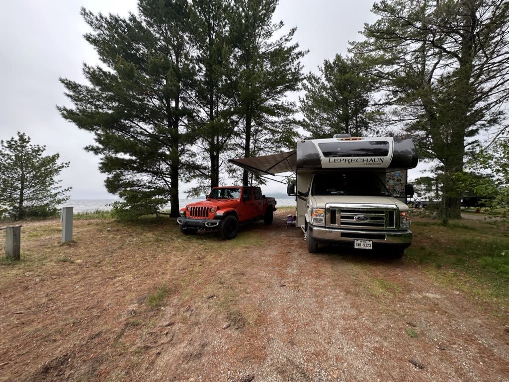 A red jeep and a white RV parked under trees.