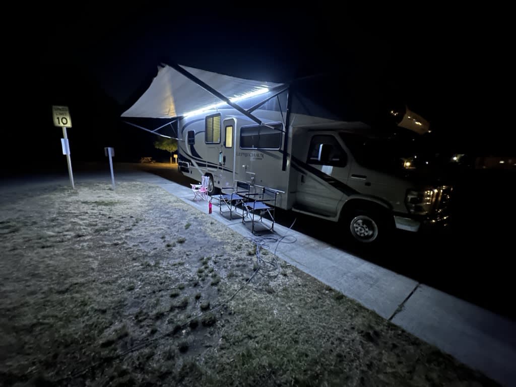 An RV parked at night with an extended awning and outdoor seating.