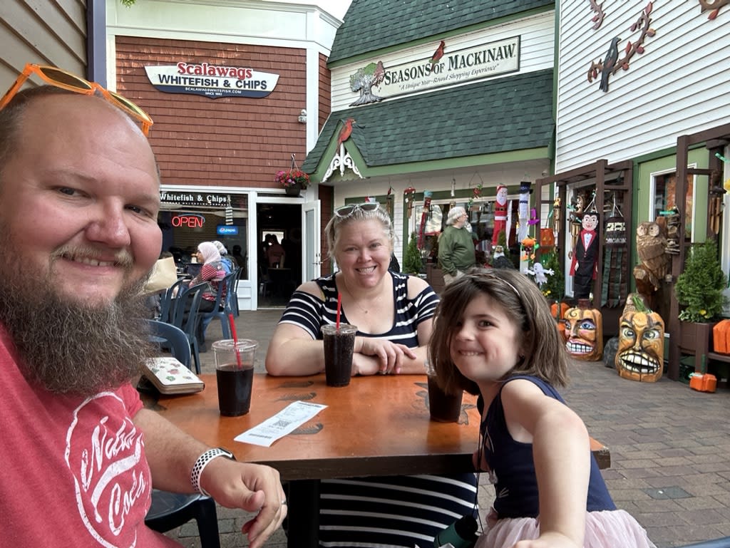 Three people sitting at a table with drinks outside a restaurant.