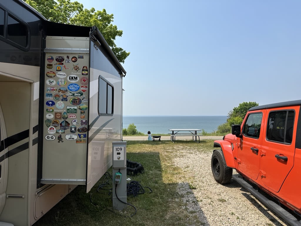 View of a campsite with an RV and a jeep by the lakeside.