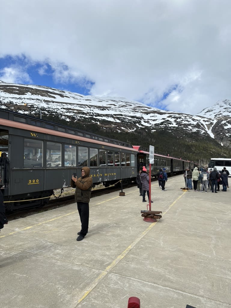 Train station with passengers near snowy mountains.