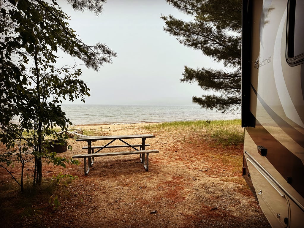 A picnic table by the shore near a camper.