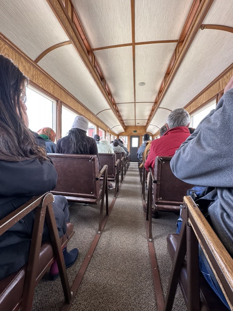 Interior of a train car showing seated passengers.