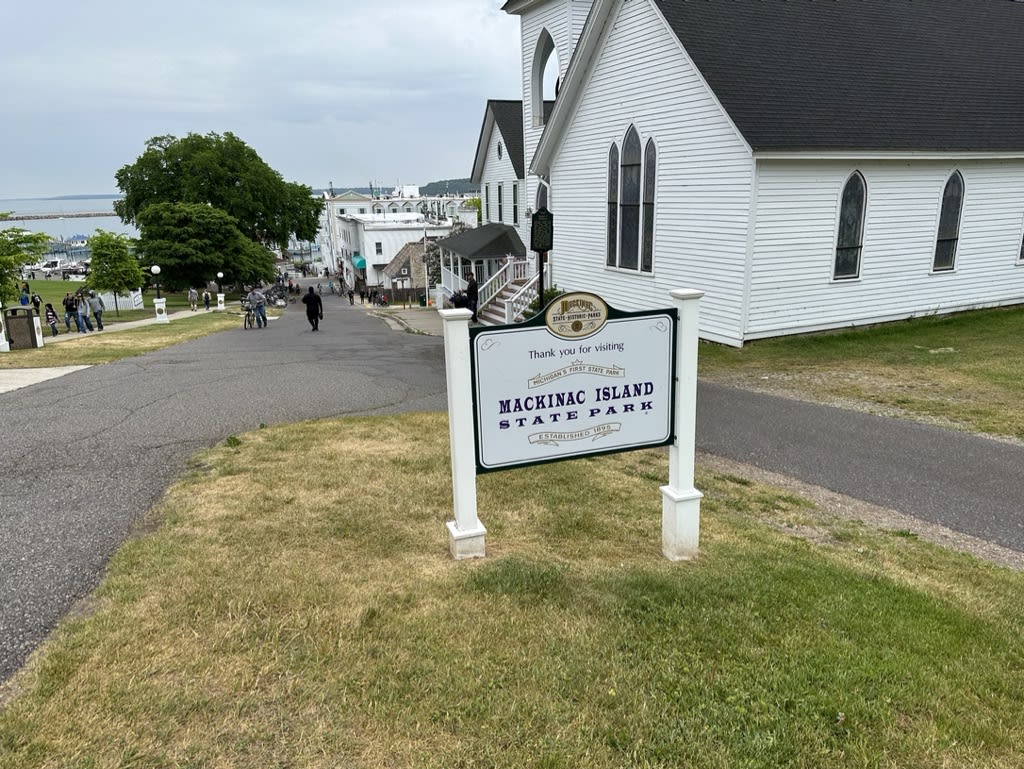 Mackinac Island State Park sign on a path with people walking and trees in the background.
