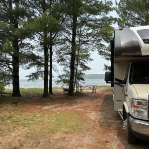 Camper parked by a lake amid pine trees.