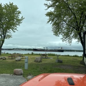 A landscape view of a river with a large ship, trees, and picnic tables.