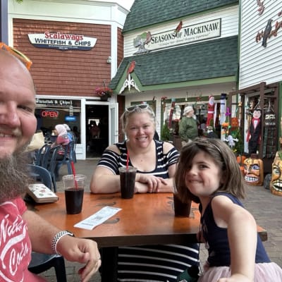 Three people sitting at a table with drinks outside a restaurant.