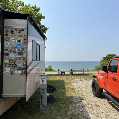 View of a campsite with an RV and a jeep by the lakeside.