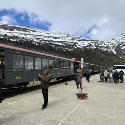 Train station with passengers near snowy mountains.