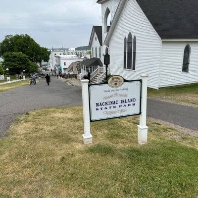 Mackinac Island State Park sign on a path with people walking and trees in the background.