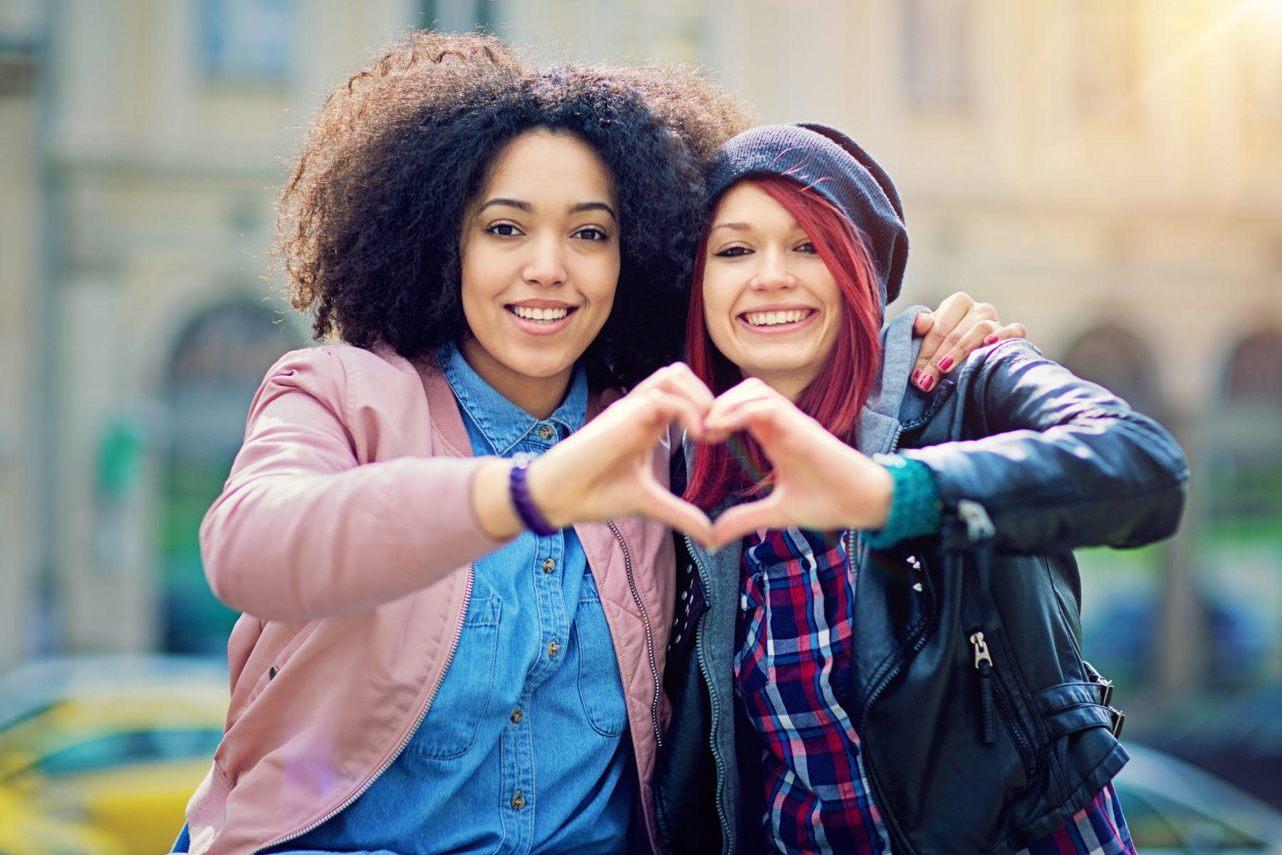 Two girlfriends making heart with their hands on the street