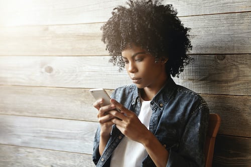 Young female hipster looking away while using mobile phone against