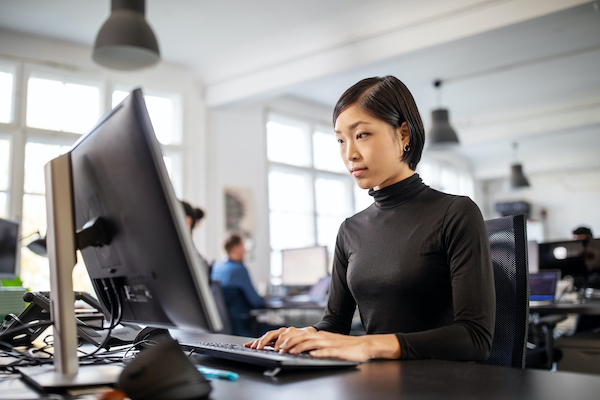 Woman busy working at her desk in open plan office Businesswoman working on desktop computer with colleagues in background. Female executive busy working at her desk in open plan office.