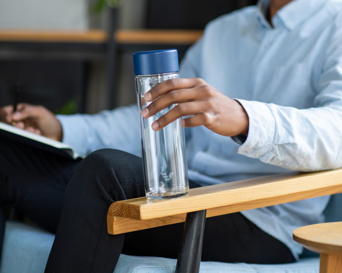 Male sitting in chair holding an Ever Vessel Glass Multi Blue water bottle
