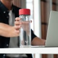 Man holding an Ever Vessel Glass Multi with a  Red lid filled with water on a desk