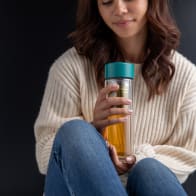 Female holding an Ever Vessel Glass Multi tea flask with Teal green lid and green tea inside