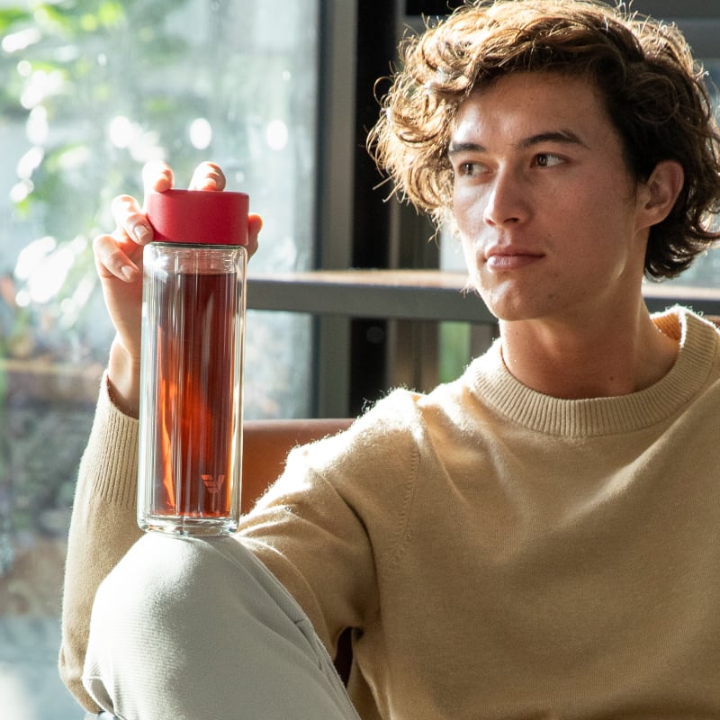 Male holding an Ever Vessel Glass Multi tea flask bottle with Red colored lid and black infused tea inside