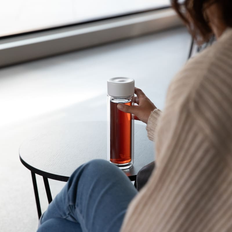 Female holding an Ever Vessel Glass Multi tea flask bottle with White Sand colored lid and black infused tea inside