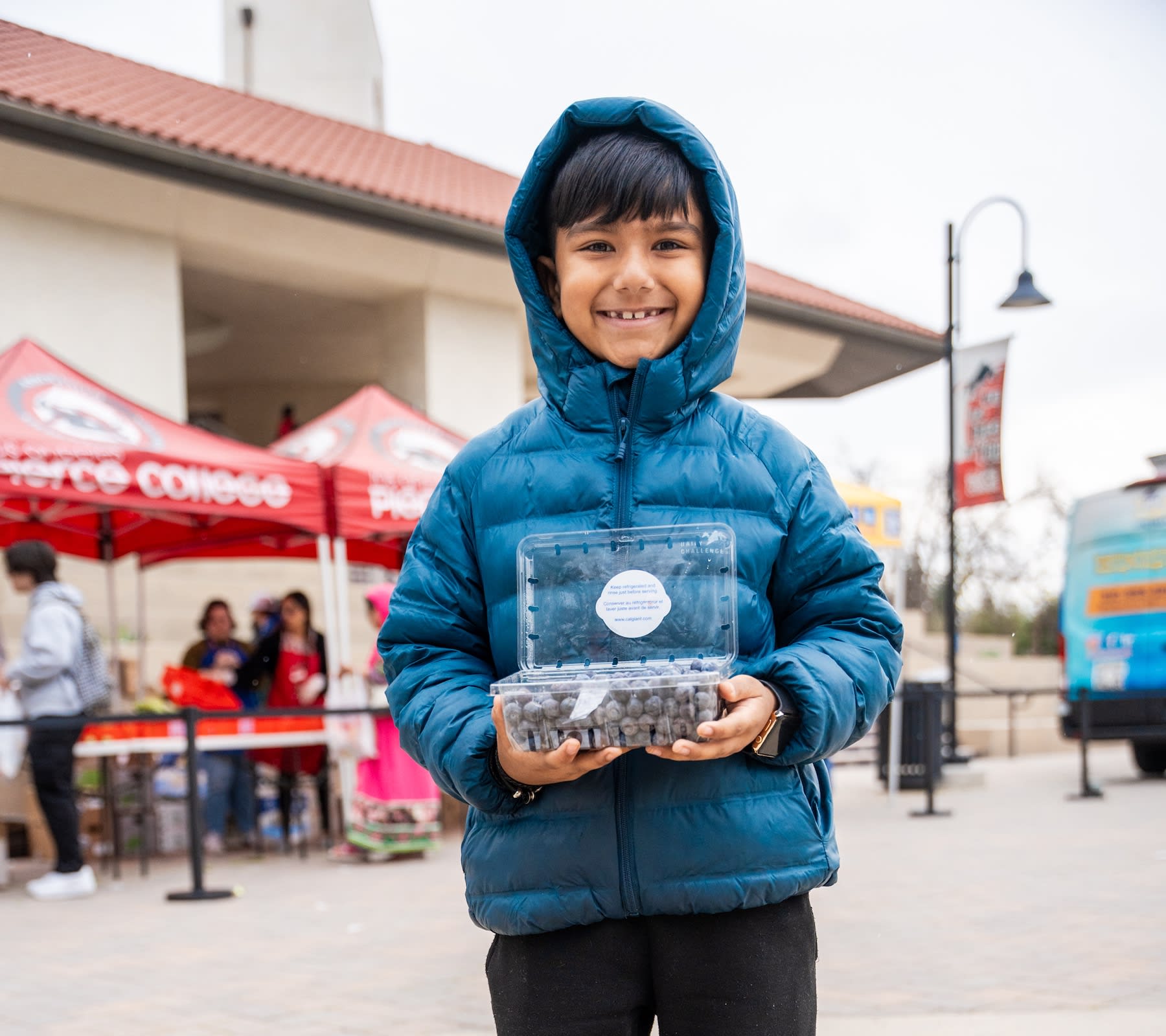 Young boy in a blue jacket holding blueberries while grinning.