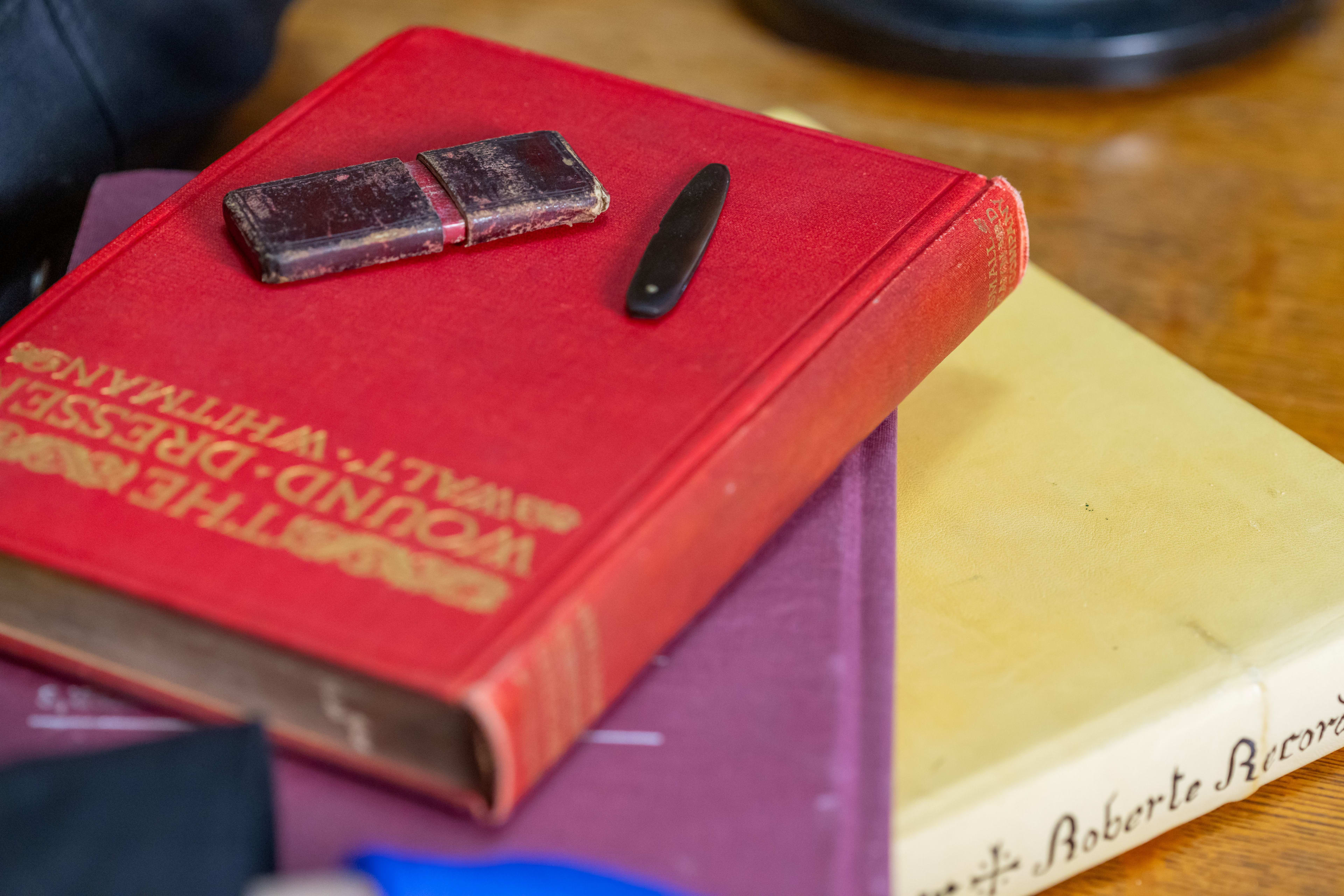 A pile of old books with a lancet case and closed lancet on top of a red book. 