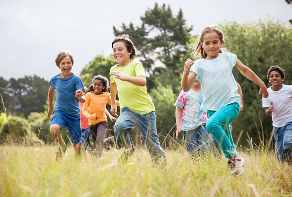 Group of diverse boys and girls running through a field with joyful looks on their faces.
