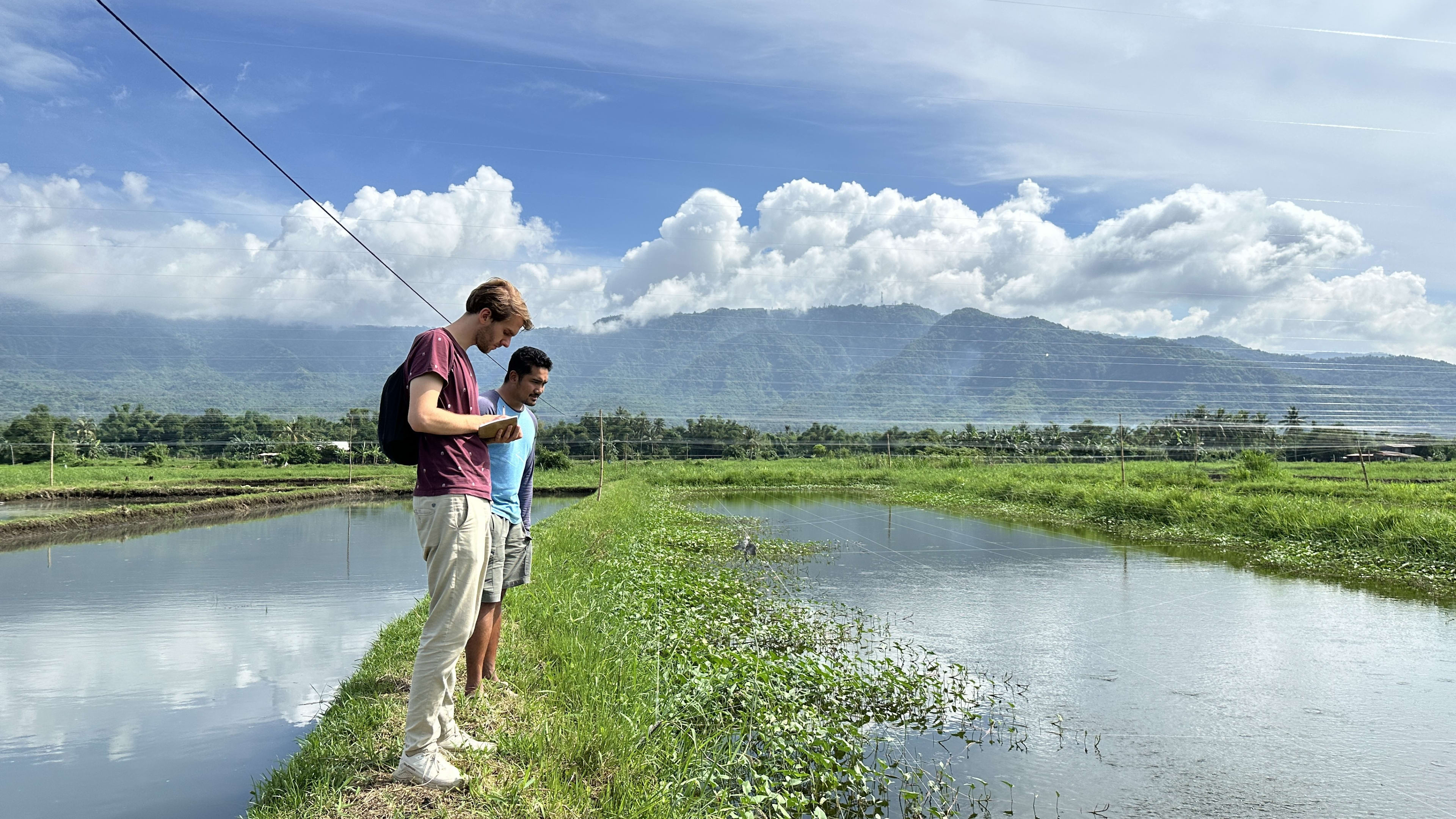 Two individuals looking at a fish pond standing in front of a mountain