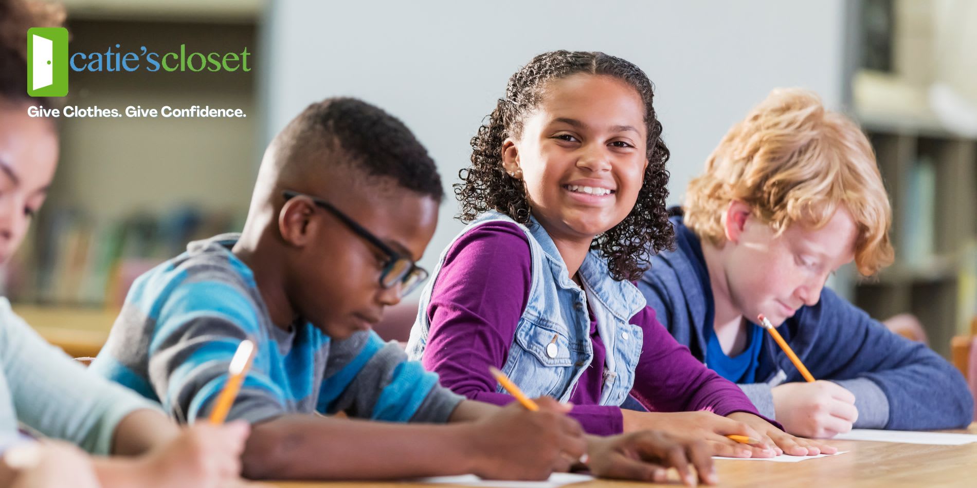kids in classroom writing. one girl looking up smiling at the camera.