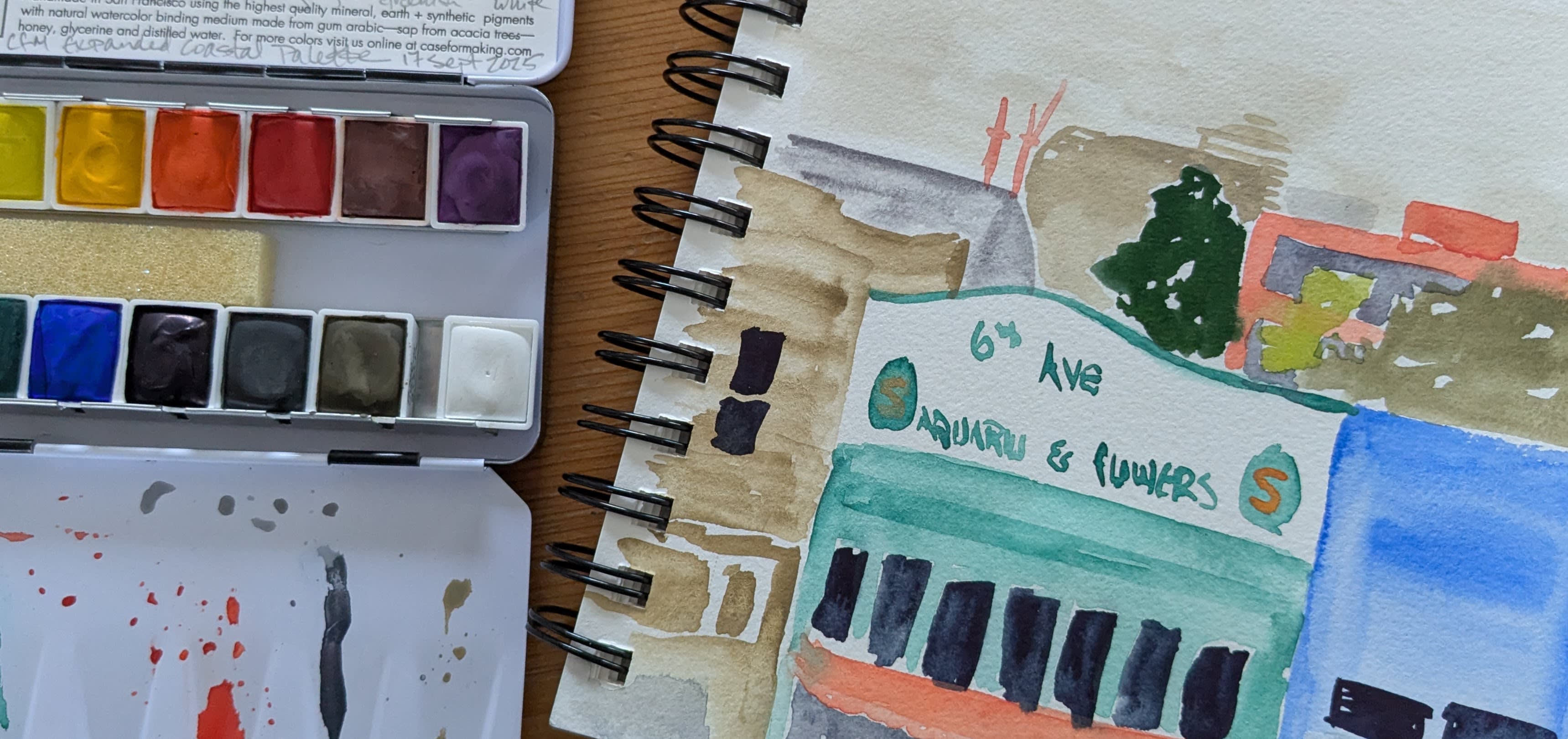 Close-up image of a small watercolor palette and a painting in a spiral-bound notebook of the fog-filled Inner Richmond neighborhood of San Francisco. 