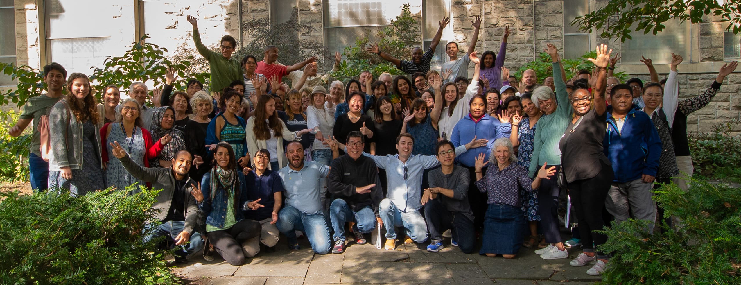 a large, diverse group of adult English language students smiling and waving