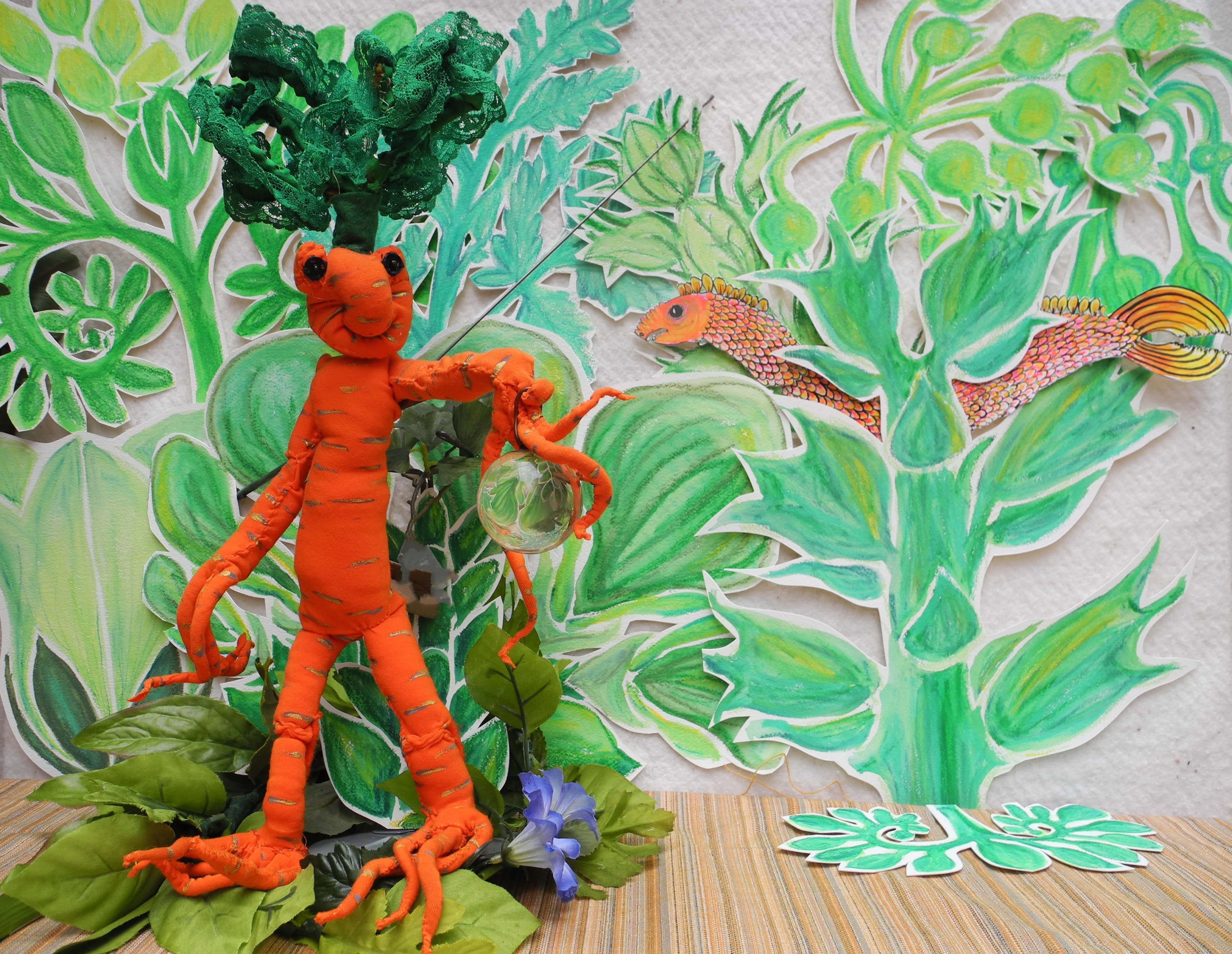 A soft sculpture orange humanoid carrot puppet holds an orb. 